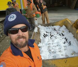 Expeditioner self captured photo in front of excavator bucket filled with snow and beverages.