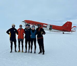 five expeditioners standing on the snow in front of a basler aircraft
