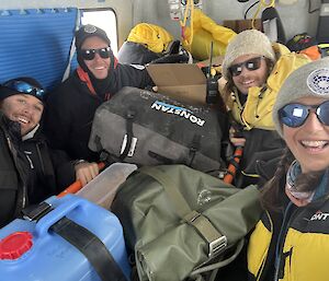 Four smiling expeditioners and their supplies in the back of a Hagglunds vehicle