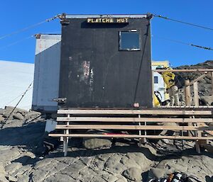 A Beaten up old hut on a rocky mound surrounded by ice.