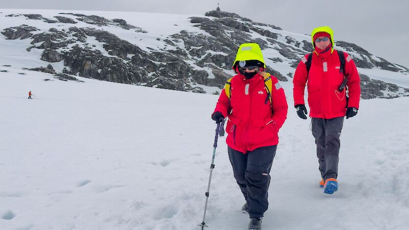 Two people in red walk across a snowy slope