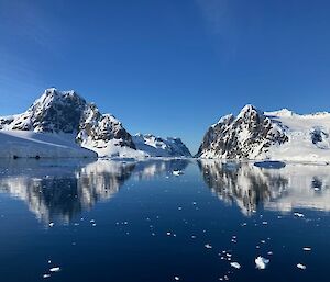 Rocky, snow-covered mountains with still water in the foreground.