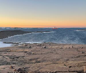 The red icebreaker in the distance with water and the rocky land in the foreground.