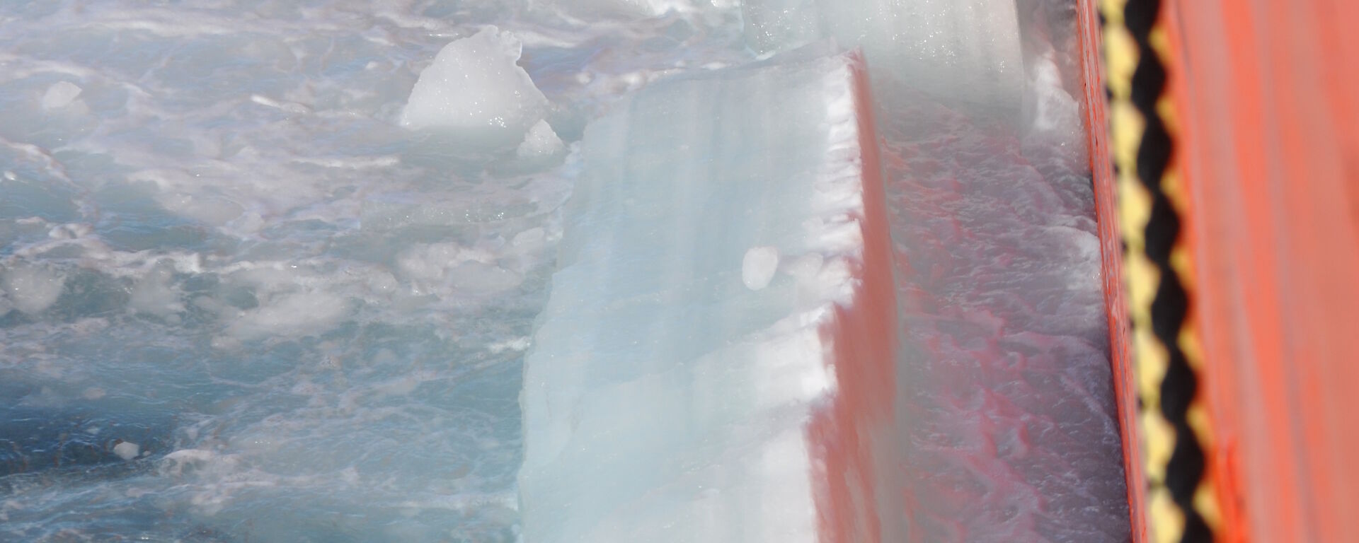 Side view of an orange ship, breaking through thick sea ice.