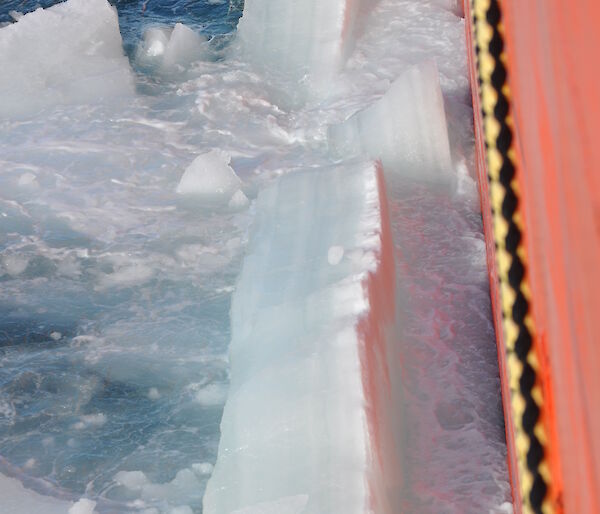 Side view of an orange ship, breaking through thick sea ice.