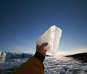 A hand holding up some sea ice to the sun.