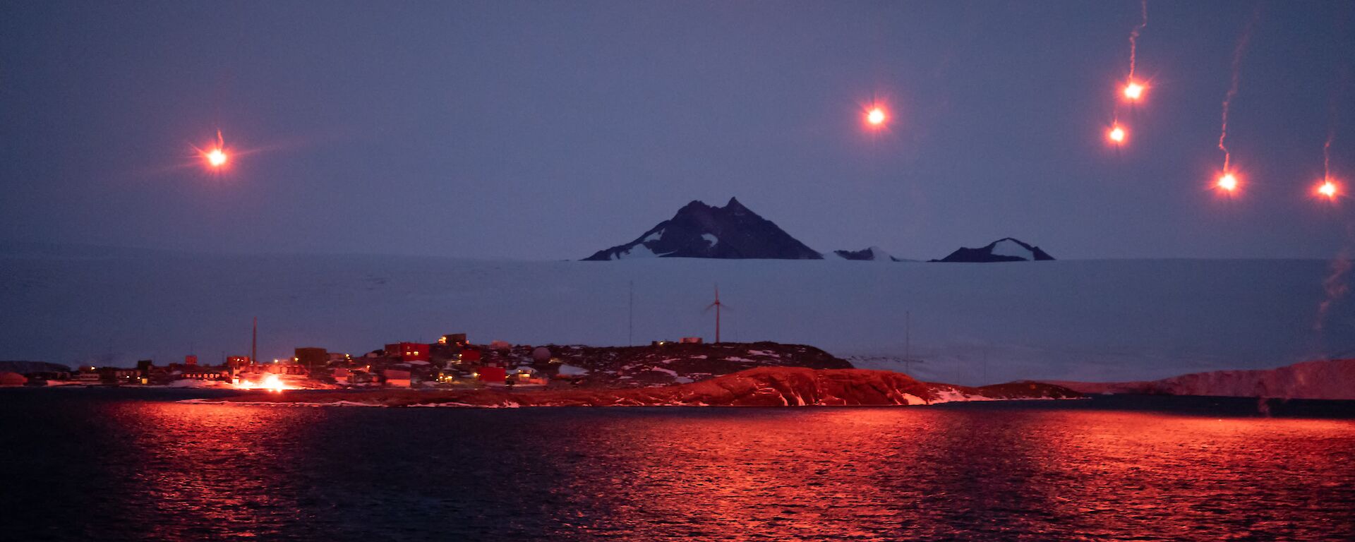 Seven bright pink flares light up the sky and station at Mawson - as viewed from the ship