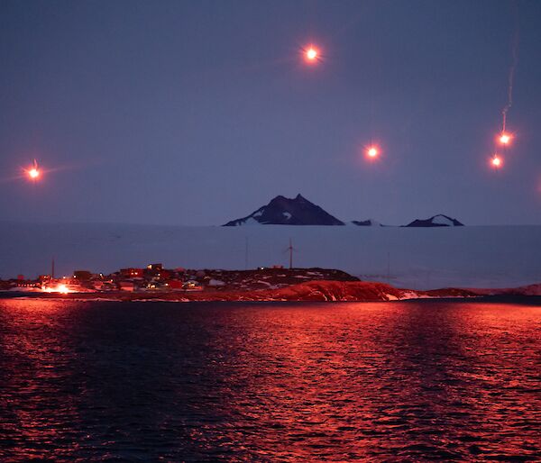 Seven bright pink flares light up the sky and station at Mawson - as viewed from the ship
