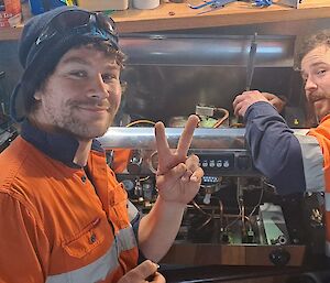 Two men in high vis work on a coffee machine.