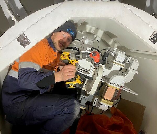 A man in orange high vis sits in a confined space with equipment.