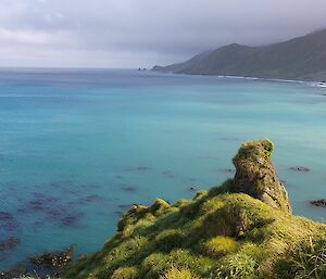 Huge green bay with a yacht moored to the left and steep island cliffs to the right.