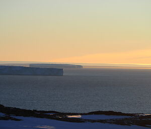 Golden glow of sunset with a still sea in the foreground and icy headlands stretching out into the bay.