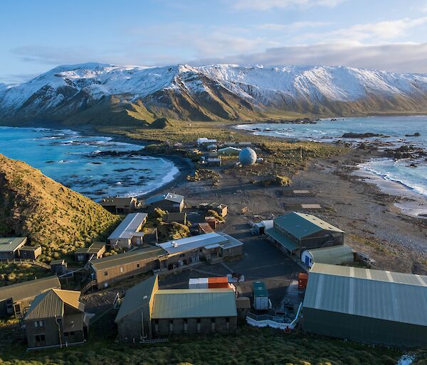 Snow-capped ridge in the background, Macquarie island station buildings in the foreground.
