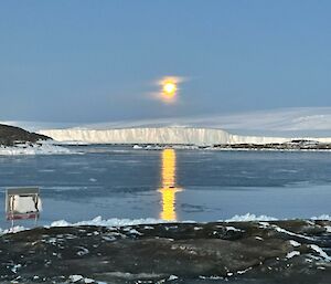 A bright full moon with a few wispy clouds shines down forming a golden path across the freezing ocean surface