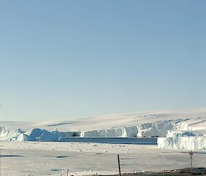 a view taken on a blue sky day of ice cliffs to the east of station with a new iceberg visible in the bay