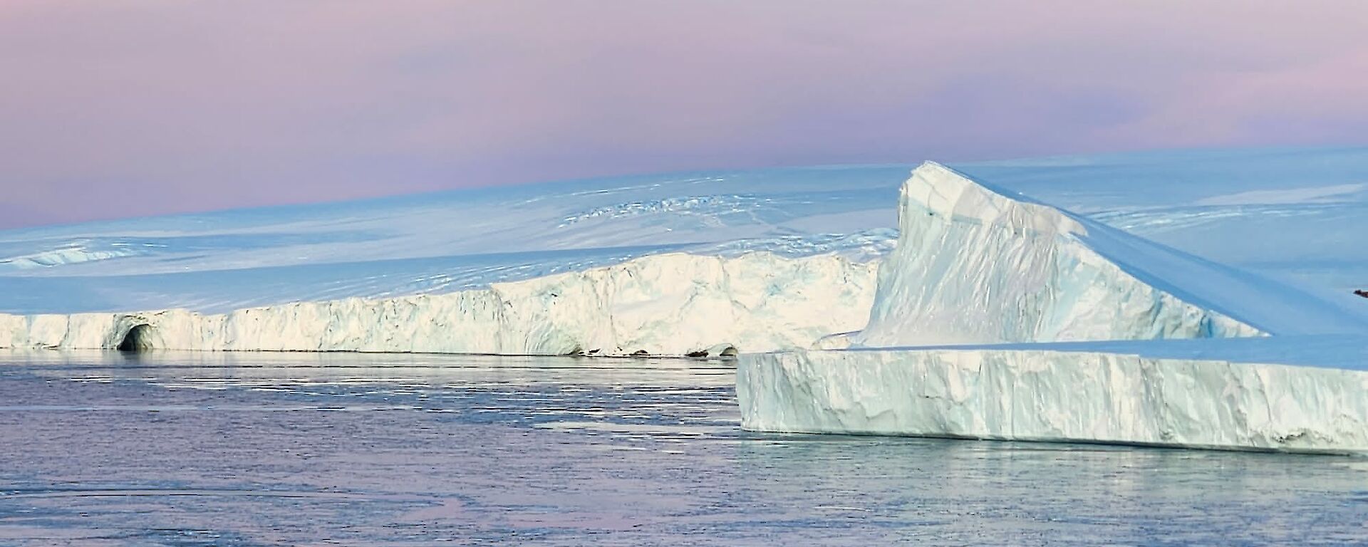 A view along the coast to the east from Mawson station. The sky is a beautiful pink purple hue typical of clear skies as the sun goes down in winter