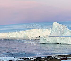 A view along the coast to the east from Mawson station. The sky is a beautiful pink purple hue typical of clear skies as the sun goes down in winter