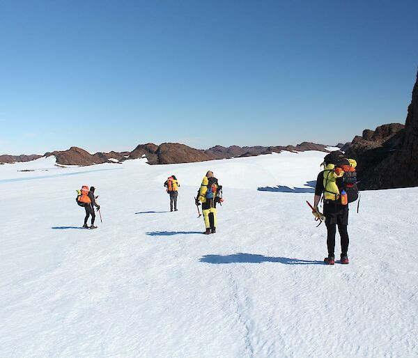 four figures in expeditioner gear on a snowy flat with rocks around