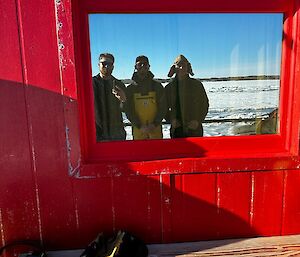 Three people looking through a window pain in the red hut