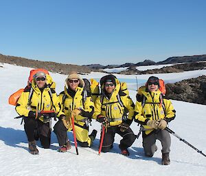 Four people crouch down for a photo on a glacier