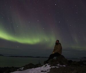 A lone figure on a rock observes and aurora australis