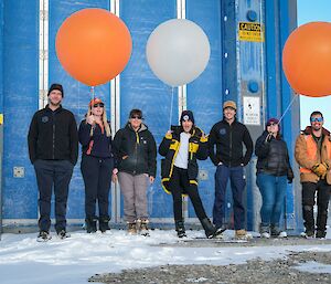 Seven expeditioners of Bureau of Meteorology pose for a photo in front of the balloon release building.