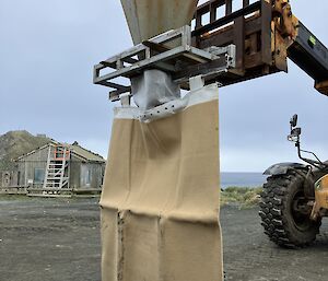 A tractor is lifting up a hessian bag to fill with sand