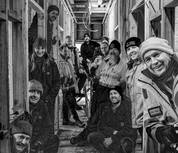 A black and white image with thirteen people standing down either side of a hallway under construction