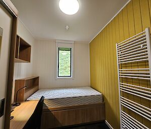 Inside of a bedroom. There is a small bedroom with a bed, towel rack, desk and small window