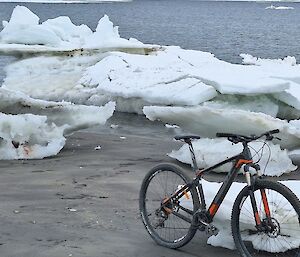 A bicycle propped up against a large piece of ice, with a body of water in the background