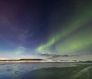 Purple and green auroral fronts across the sky lighting up newly formed pancake ice in the harbour in front of Mawson station on 25 March 2024