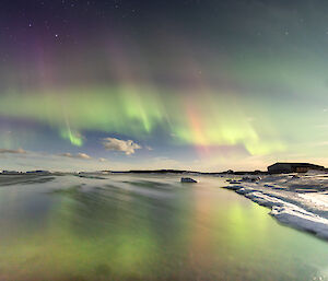 The night sky above Horseshoe Harbour near Mawson station filled with green and purple aurora along with a flash of orange red on 25 March 2024