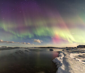 A fantastic view of a sky full of green yellow purple red auroral colour above Horseshoe Harbour near Mawson station on 25 March 2024, the light reflected in the still harbour waters