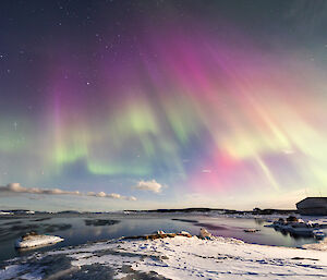 A sky full of auroral light playing green yellow orange red and purple against the backdrop of stars above Mawson station on 25 March 2024