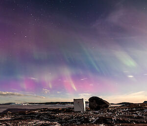 Purple and green auroral lights in bands across the sky with the explosives container on East arm in the foreground at Mawson station