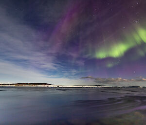 Purple and green auroral light appearing to rain down upon the harbour in front of Mawson station