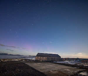 Purple green aurora in the sky with the old hangar at Mawson in the foreground