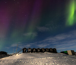 Reddish purple curtains of auroral light fringed with green above the fuel tanks at Mawson station on 25 March 2024