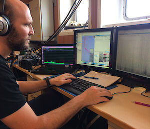 A man wearing headphones looking at two computer monitors showing sound signals from the ocean.