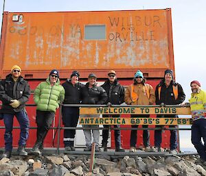 A group of people stand in front of an orange hut