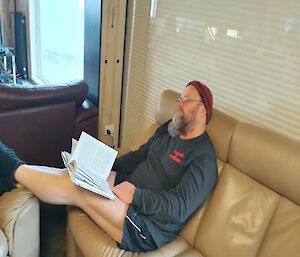 A man holding  a book asleep on a couch