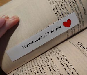 A book, open, with a bookmark inside saying "Thanks again, I love you".
