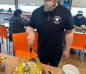 A smiling man wearing a beanie cuts a cake