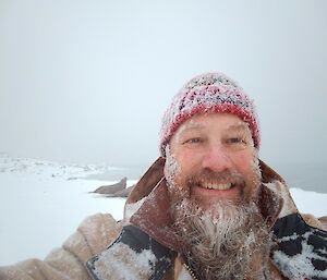 A bearded smiling man, wearing a beany, with snow everywhere