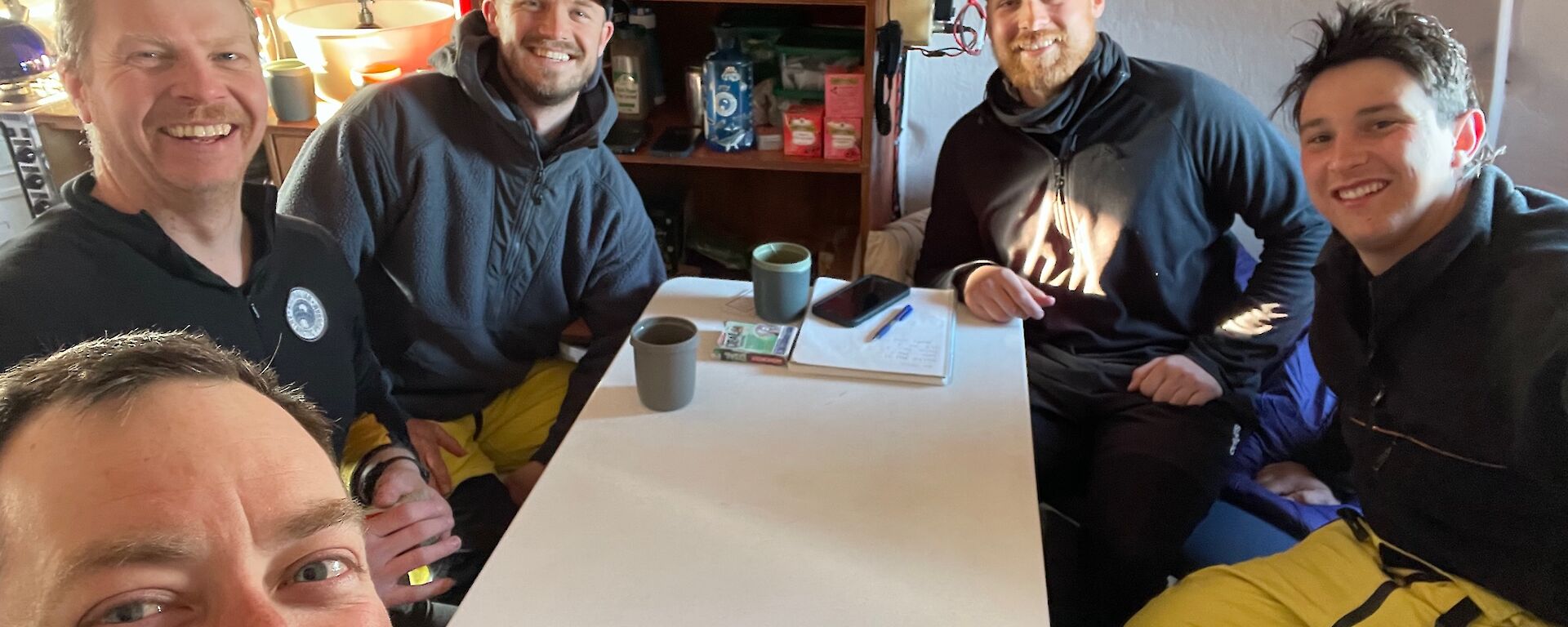 Expeditioners sit around a table at Brookes Hut