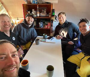 Expeditioners sit around a table at Brookes Hut