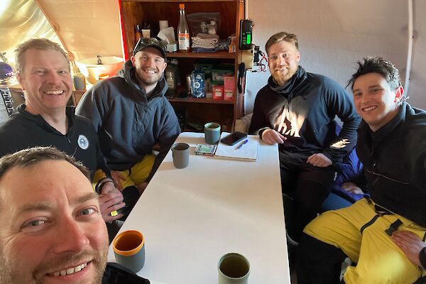 Expeditioners sit around a table at Brookes Hut