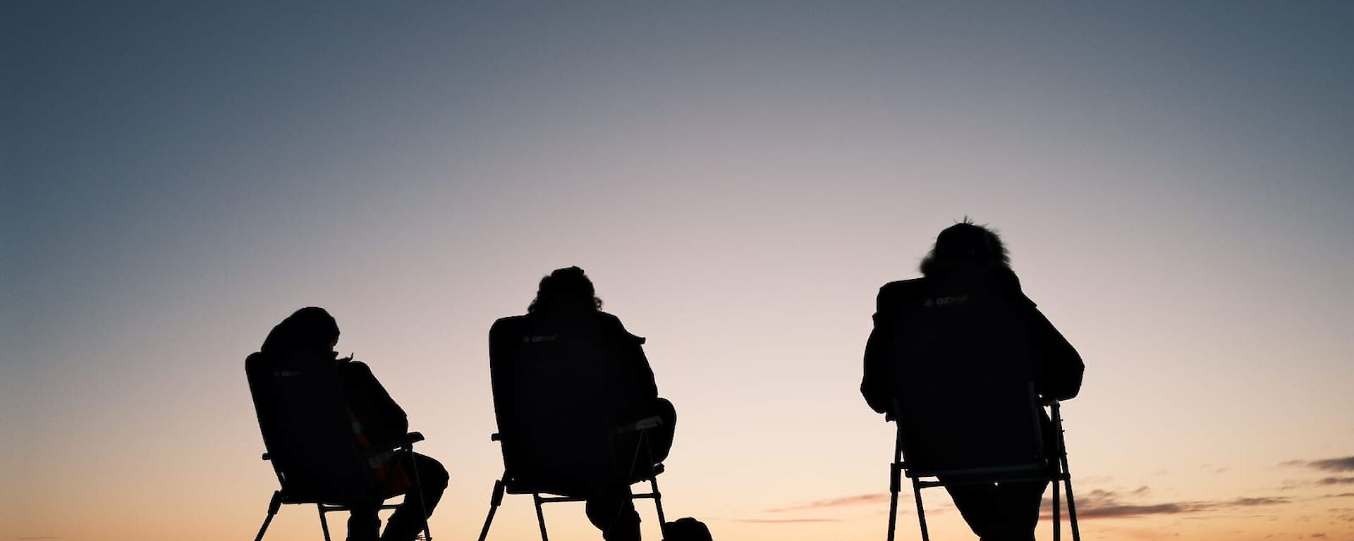 Three expeditions sitting of fold out chairs watching the sun set below the horizon