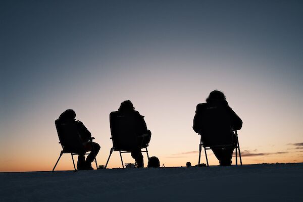 Three expeditions sitting of fold out chairs watching the sun set below the horizon