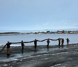Expeditioners carrying part of the fuel line, used during refuelling recently, back to Mawson for safe storage over the winter.